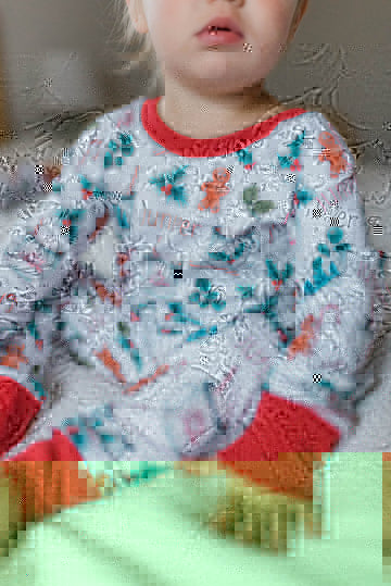 baby girl wearing personalized Christmas PJ's with images of hot cocoa, gingerbread men, and holly leaves on a white background and red cuffs.