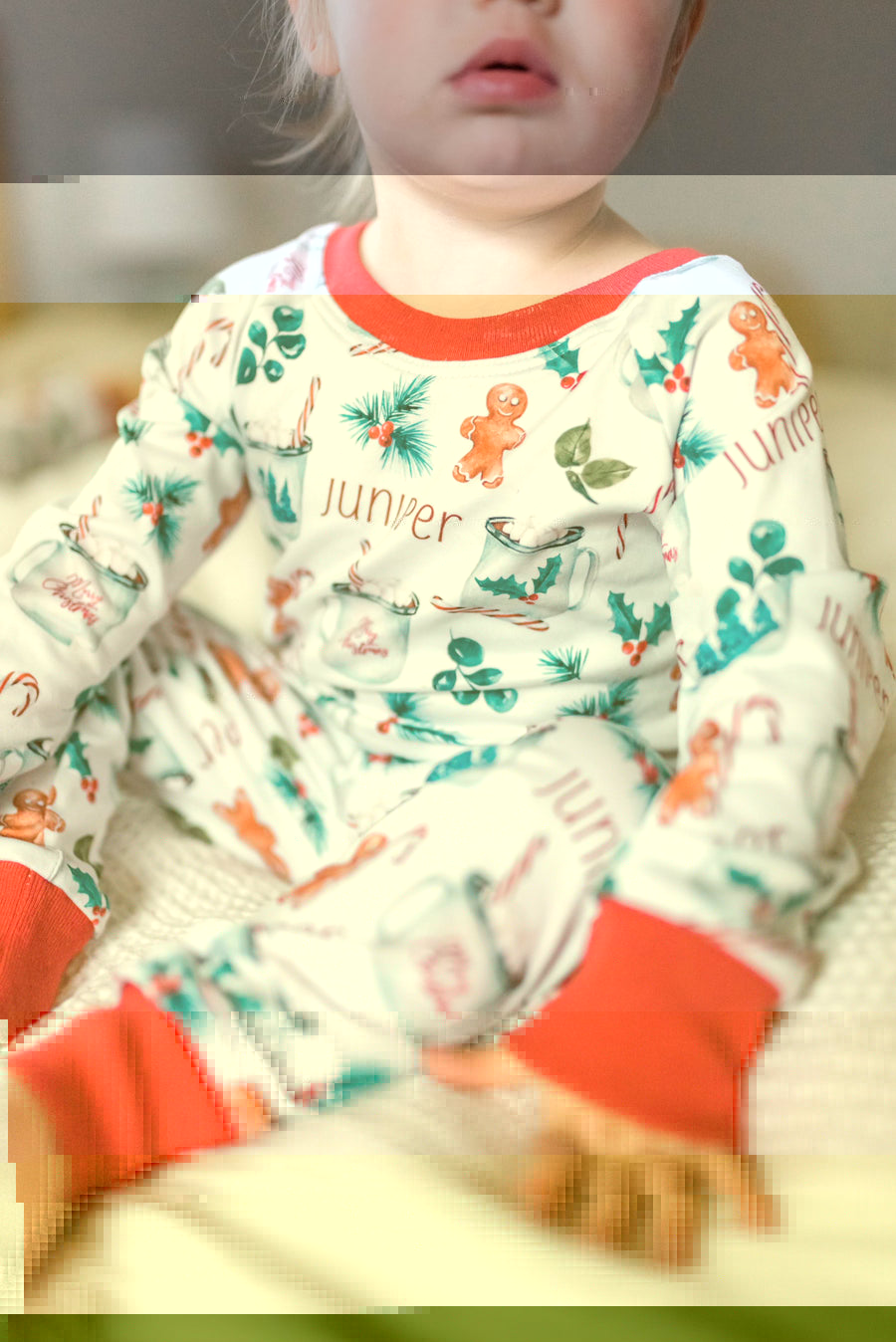 baby girl wearing personalized Christmas PJ's with images of hot cocoa, gingerbread men, and holly leaves on a white background and red cuffs.