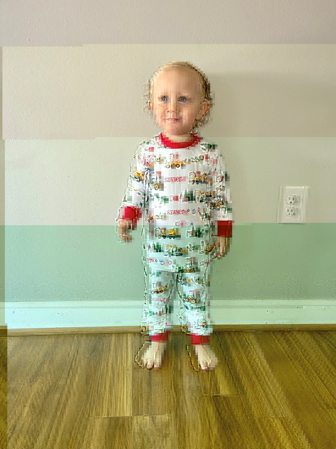 little boy wearing Christmas Construction custom holiday pajamas with construction vehicles in santa hats and christmas trees, featuring child's name in red letters and red cuffs.