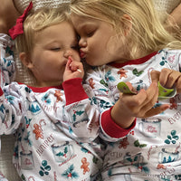 baby girl wearing personalized Christmas PJ's with images of hot cocoa, gingerbread men, and holly leaves on a white background and red cuffs.