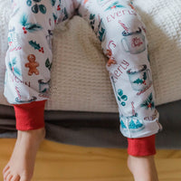 baby girl wearing personalized Christmas PJ's with images of hot cocoa, gingerbread men, and holly leaves on a white background and red cuffs.